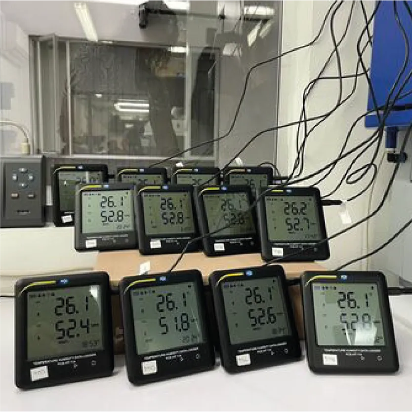 Laboratorio Temperatura | ONAC | Higielectronix Colombia Row of digital environmental meters on a lab bench showing ~26.1°C and ~52% humidity, with cables and glass enclosure in the background.
